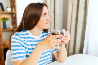 Evin penceresinin yanında çay içen genç ve güzel bir kadın..