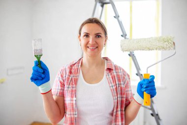 İnsanların tadilatı ve ev tadilatı. Odanın duvarlarını boyadıktan sonra kirli silindir tutan ve fırçalayan olumlu tatmin olmuş kadın.