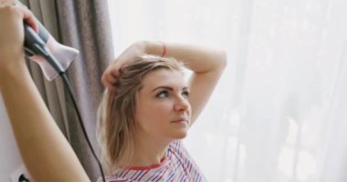 Genç bir kadın uzun saçını elektrikli saç kurutma makinesiyle kurutuyor. Yüksek kalite 4k görüntü