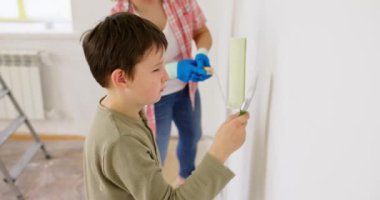 Anne ve oğlu boya silindiri ve fırçayla duvar boyuyor, birlikte tadilatın keyfini çıkarıyorlar. Ailecek vakit geçireceğiz. Kalacak yer ve aile kavramı. Yüksek kalite 4k görüntü