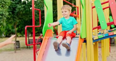 Mutlu anne ve küçük oğlu oyun parkı kaydırağında oynuyorlar ve parkta eğleniyorlar. Çocuklar için sağlıklı bir yaz aktivitesi. Yüksek kalite 4k görüntü