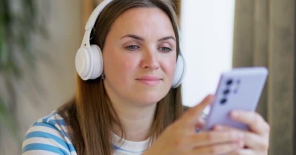坐在无线耳机里的女人在家里的休息室里听音乐 周末在室内 家庭休闲 高质量的4K镜头 — 图库视频影像