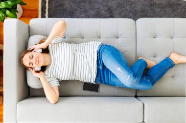 Modern kablosuz kulaklıklı huzurlu kadın rahat bir koltukta uzanıyor, müzik dinliyor. Mutlu sakin kadın kulaklık takıyor rahat bir koltukta dinleniyor, kaliteli sesin tadını çıkarıyor.