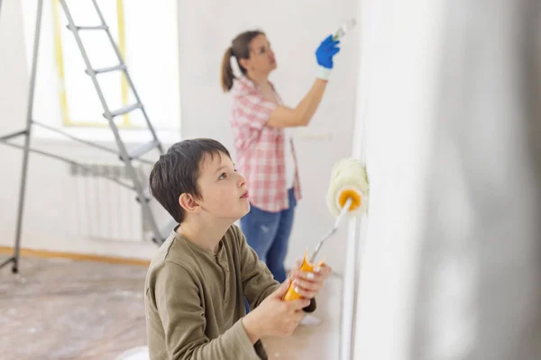 幸せな家族の母親と子供の息子はローラーとブラシを使用して塗料で壁をペイントします アパートの修理 — ストック写真