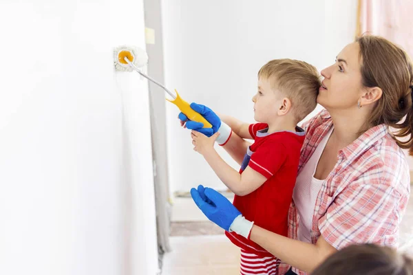 幸せな家族の母親と子供の息子はローラーとブラシを使用して塗料で壁をペイントします アパートの修理 — ストック写真