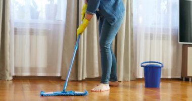 Günlük kıyafetli genç bir kadın, tahta zemini ıslak bir mikrofiber paspasla yıkıyor, ödev yapıyor, rutin temizlik yapıyor, temizlik yapıyor. Yüksek kalite 4k görüntü
