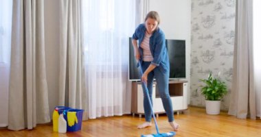 Günlük kıyafetli genç bir kadın, tahta zemini ıslak bir mikrofiber paspasla yıkıyor, ödev yapıyor, rutin temizlik yapıyor, temizlik yapıyor. Yüksek kalite 4k görüntü