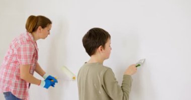 Anne ve oğlu boya silindiri ve fırçayla duvar boyuyor, birlikte tadilatın keyfini çıkarıyorlar. Ailecek vakit geçireceğiz. Kalacak yer ve aile kavramı. Yüksek kalite 4k görüntü