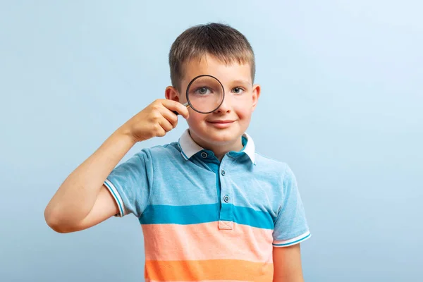 Pozytywny Ciekawski Uczeń Luźnych Ubraniach Patrzy Przez Lupę Niebieskie Tło — Zdjęcie stockowe