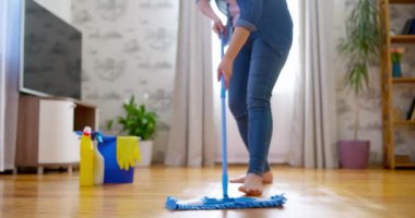 Günlük kıyafetli genç bir kadın, tahta zemini ıslak bir mikrofiber paspasla yıkıyor, ödev yapıyor, rutin temizlik yapıyor, temizlik yapıyor. Yüksek kalite 4k görüntü