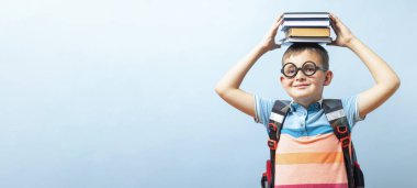 Mavi arka planda, elinde kitaplarla gözlüklü, komik gülümseyen okul çocuğu.