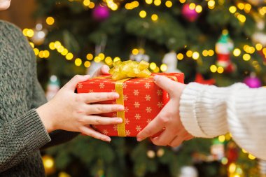 Noel ağacı arka planında çocuğa Noel hediyesi veren ebeveynlerin elleri. Noel konsepti