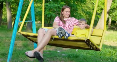 Mutlu aile, anne ve çocuk şehir parkında salıncakta sallanıyor. Mutlu aile kavramı, hayaller, eğlence. Anne ve oğul birlikte. Yüksek kalite 4k görüntü