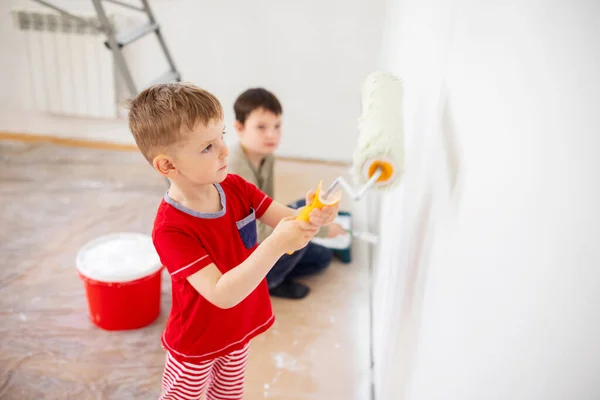 stock image Children paint a wall with brush and roller in white color. Children paint a wall.