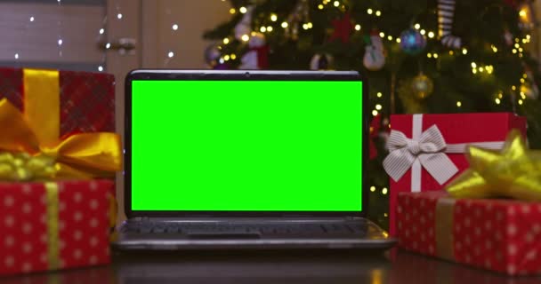 クリスマスツリーの背景にテーブルの上の贈り物に囲まれた緑の画面を持つノートパソコン クリスマスの概念のためのオンラインギフトショッピング 年末年始 高品質4K映像 — ストック動画