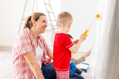 Çocuklarıyla birlikte mutlu bir aile annesi duvarları silindir ve fırçayla boyuyor. Dairede tamirat var.