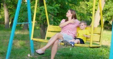 Mutlu aile, anne ve çocuk şehir parkında salıncakta sallanıyor. Mutlu aile kavramı, hayaller, eğlence. Anne ve oğul birlikte. Yüksek kalite 4k görüntü