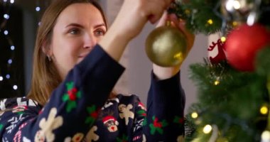 Genç bir kadın, şenlikli iç mekanıyla rahat oturma odasında Noel ağacını süslüyor. Mutlu Noeller ve mutlu yıllar. Yüksek kalite 4k görüntü