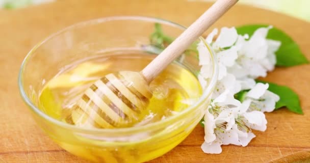 蜂蜜从蜂蜜搅拌器中滴落在木桌上的玻璃碗里 健康的有机蜂蜜从木制蜂蜜汤匙中浸出 高质量的4K镜头 — 图库视频影像