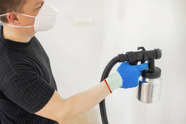 Koruyucu maskeli, duvarları sprey silahla boyayan bir işçi. Dairenin duvarını boyuyorum. Onarım kavramı