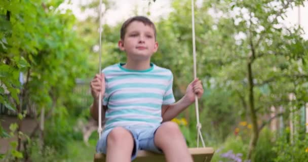 庭でスイングに揺れる幸せな男の子 子供は木の子供時代の夢の上で木製のスイングで遊ぶ 高品質4K映像 — ストック動画