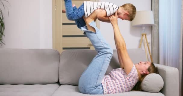 Mutlu Anne Kanepeye Uzanıp Çocuğuyla Eğleniyor Heyecanlı Çocuğu Bacaklarıyla Havaya — Stok video