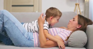 Anne, oturma odasındaki kanepede yan yana yatarken küçük tatlı oğlunu kucaklıyor ve öpüyor. Yüksek kalite 4k görüntü