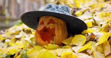 Sonbaharda düşen sarı yapraklara oyulmuş gözleri ve ağzı olan korkunç Cadılar Bayramı balkabağı şapkası. Yüksek kalite 4k görüntü