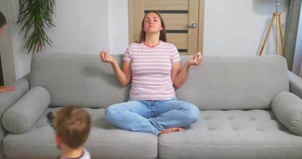 Мать Медитирует Сидя Диване Время Активные Энергичные Дети Играют Бегая — стоковое видео