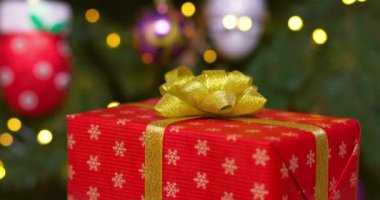Altın kurdeleli kırmızı bir kutu ve bir fiyonk yanıp sönen çelenk ışıklarıyla bir Noel ağacının arka planında dönüyor. Yüksek kalite 4k görüntü