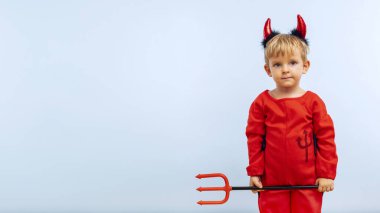 Mavi arka planda mızrak olan şeytan kostümlü neşeli çocuk. Cadılar Bayramı partisi konsepti. Web pankartı.