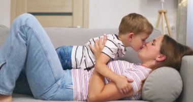 Anne, oturma odasındaki kanepede yan yana yatarken küçük tatlı oğlunu kucaklıyor ve öpüyor. Yüksek kalite 4k görüntü