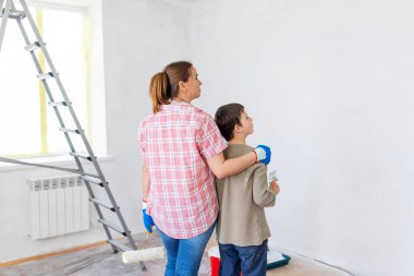 Mutlu bir aile babası ve çocuğu. Duvarı silindir ve fırçayla boyuyor. Dairede tamirat var.