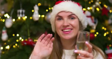 Noel Baba şapkalı gülümseyen kadın ailesine ya da ekrandaki arkadaşlarına en iyi dileklerinin şampanya kadehiyle kadeh kaldırmak olduğunu söylüyor. Heyecanlı kadın Noel 'de arkadaşlarını uzaktan selamlıyor