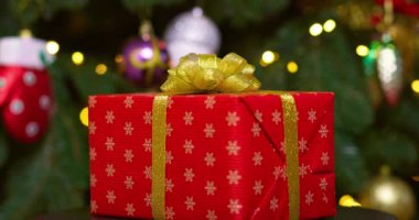 Altın kurdeleli kırmızı bir kutu ve bir fiyonk yanıp sönen çelenk ışıklarıyla bir Noel ağacının arka planında dönüyor. Yüksek kalite 4k görüntü