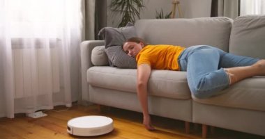 Robot elektrikli süpürge yerde çalışırken evdeki kanepede uyuyan çok yorgun bir kadın. Yüksek kalite 4k görüntü