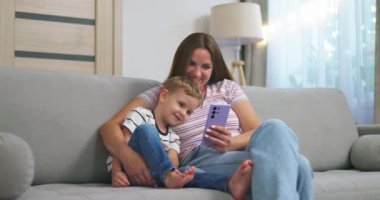 Kadın ve küçük oğlu akıllı telefonlu rahat koltukta oturuyorlar. Aileler evde birlikte vakit geçirirler. Akıllı telefon kullanır, oyun oynar, video izler, selfie çekerler. Yüksek kalite 4k görüntü