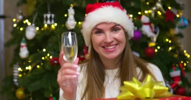 Smiling Woman Santa Hat Waves Hand Family Friends Screen Says — Stock Video