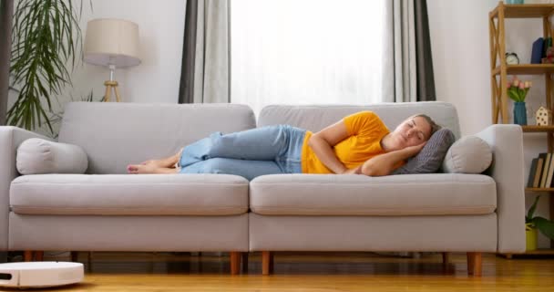 Mulher Muito Cansada Dormindo Sofá Casa Enquanto Robô Aspirador Trabalhando — Vídeo de Stock