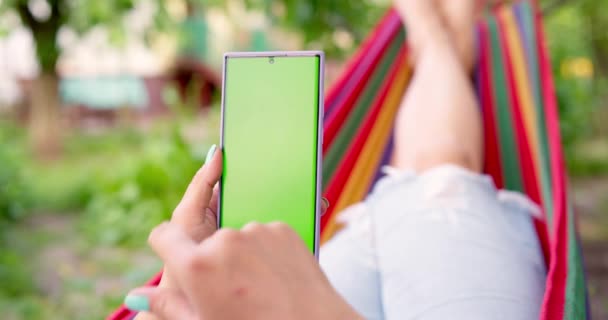 Frau Auf Einer Hängematte Garten Liegend Hält Sie Ein Smartphone — Stockvideo