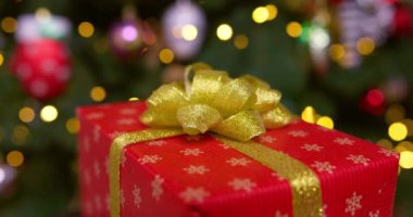 Altın kurdeleli kırmızı bir kutu ve bir fiyonk yanıp sönen çelenk ışıklarıyla bir Noel ağacının arka planında dönüyor. Yüksek kalite 4k görüntü