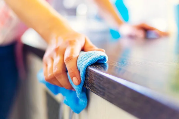 Woman hand cleaning the counter in the kitchen with a blue microfiber cloth. Household work