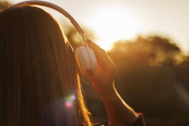 Gün batımında müzik dinleyen kulaklıklı genç bir kadın..