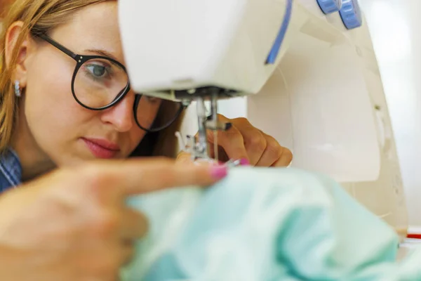 Stock image Woman seamstress in glasses works on the sewing-machine at her workplace in workshop