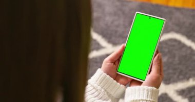 Krom tuşlu, yeşil ekranlı akıllı telefonu tutan esmerin arka planı içeriği izliyor. Kadehler ve çağdaş insanlar konsepti. Yüksek kalite 4k görüntü