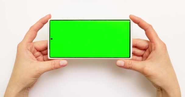ホワイトバックグラウンドで緑色の画面でスマートフォンを保持する手 高品質の4K映像 — ストック動画