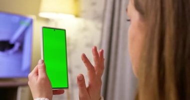 Krom tuşlu, yeşil ekranlı akıllı telefonu tutan esmerin arka planı içeriği izliyor. Kadehler ve çağdaş insanlar konsepti. Yüksek kalite 4k görüntü