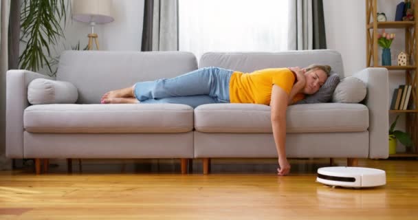 非常に疲れた女性は 床で作業するロボット掃除機をしながら 自宅でソファーで寝ています 高品質の4K映像 — ストック動画