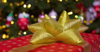 Altın kurdeleli kırmızı bir kutu ve bir fiyonk yanıp sönen çelenk ışıklarıyla bir Noel ağacının arka planında dönüyor. Yüksek kalite 4k görüntü