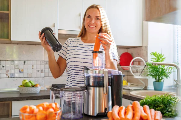 Young woman making carrot juice with juice machine at home kitchen.